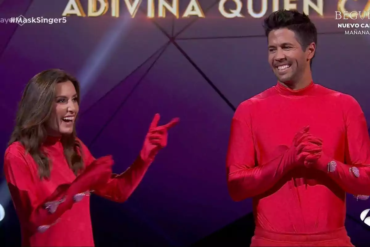 Ana Boyer y Fernando Verdasco vestidas con trajes rojos sonríen en un escenario de Mask Singer con el texto Ana Boyer y Fernando Verdasco vestidas con trajes rojos sonríen en un escenario de Mask Singer con el texto