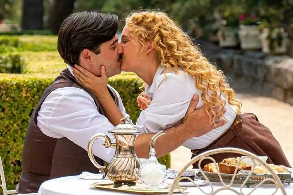 Arturo Sancho y Ana Garcés se besan apasionadamente en un jardín mientras están sentados en una mesa con un servicio de té en La Promesa.