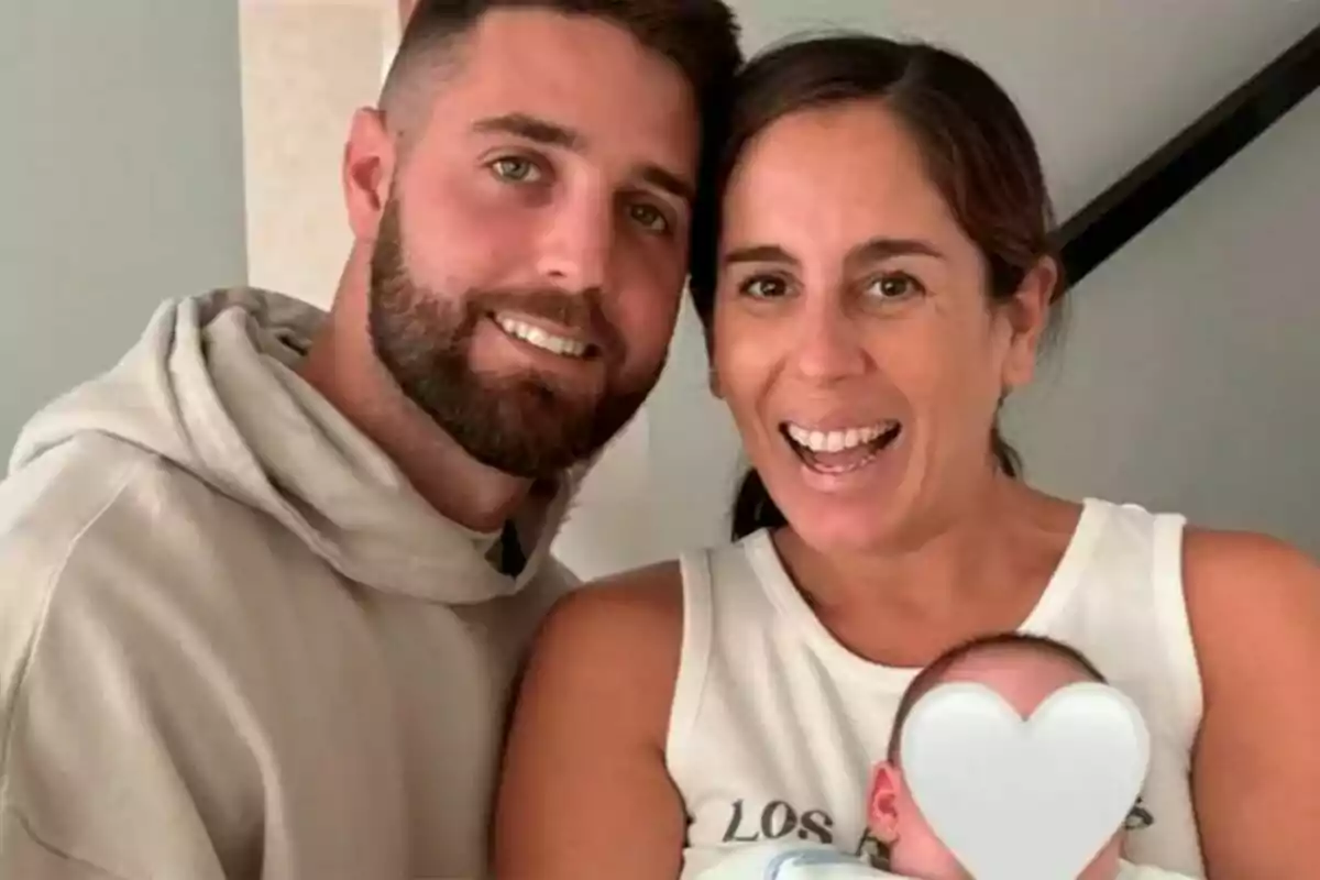 Anabel Pantoja and David Rodríguez smiling pose with a baby whose face is covered by a heart emoji.