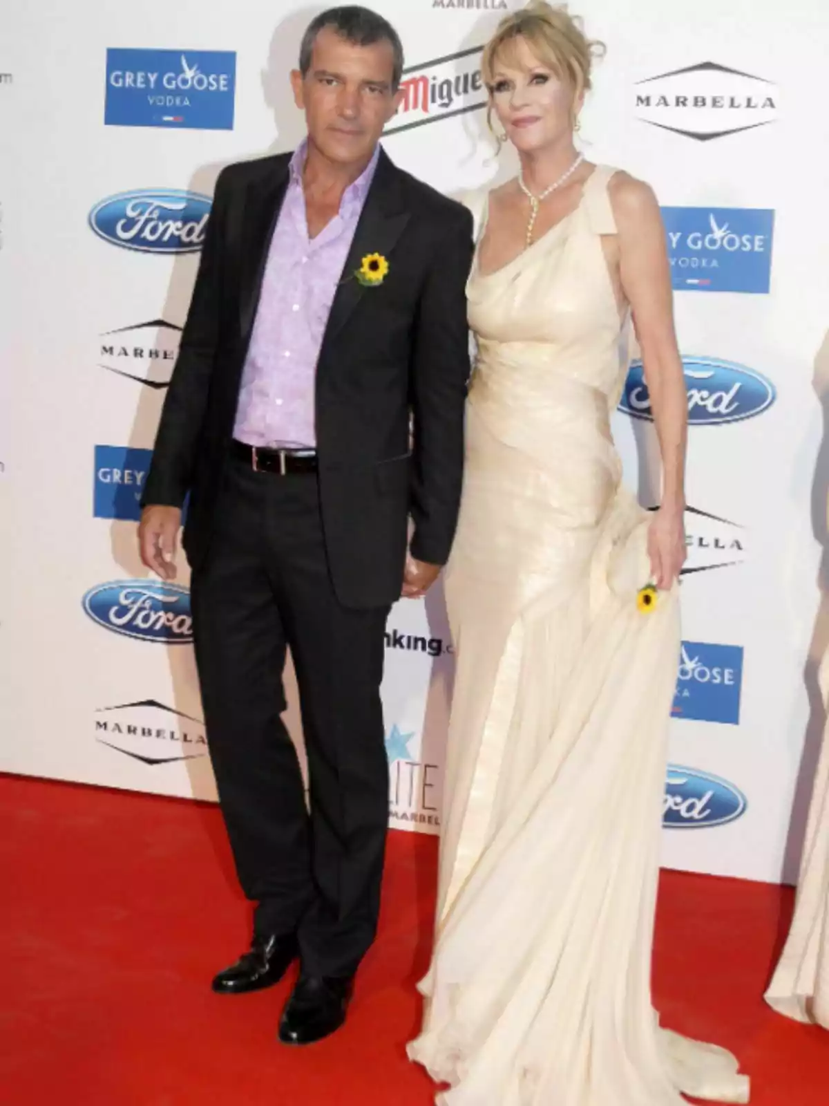 Antonio Banderas y Melanie Griffith posando en una alfombra roja con un fondo de logotipos de marcas. Antonio Banderas y Melanie Griffith posando en una alfombra roja con un fondo de logotipos de marcas.