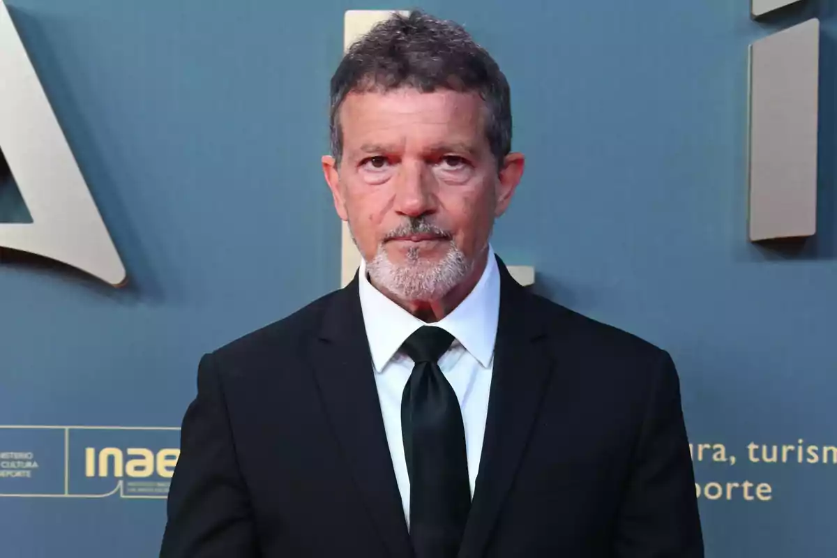 Antonio Banderas con traje negro y corbata en un evento formal con fondo azul. Antonio Banderas con traje negro y corbata en un evento formal con fondo azul.