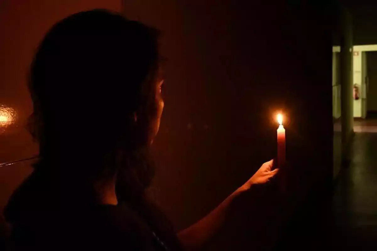 Una persona sostiene una vela encendida en un pasillo oscuro.