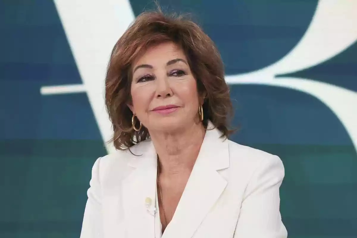 Mujer de cabello castaño y corto con chaqueta blanca y pendientes dorados en un estudio de televisión Mujer de cabello castaño y corto con chaqueta blanca y pendientes dorados en un estudio de televisión