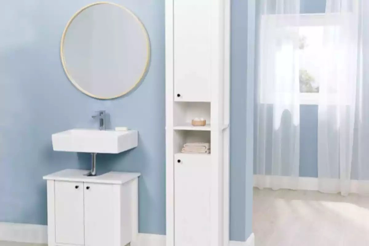 Baño moderno con paredes azules muebles blancos y un espejo redondo sobre el lavabo Baño moderno con paredes azules muebles blancos y un espejo redondo sobre el lavabo