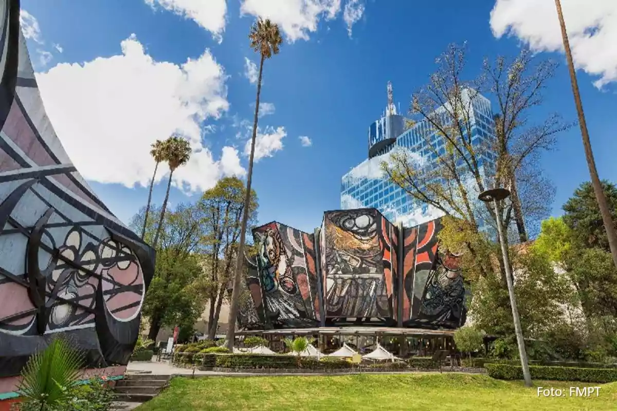 Building with colorful murals surrounded by trees and a blue sky with clouds.