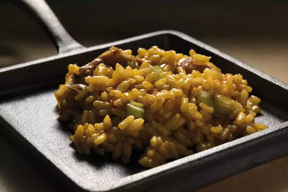 Un plato cuadrado de hierro fundido con arroz amarillo y trozos de verduras. Un plato cuadrado de hierro fundido con arroz amarillo y trozos de verduras.