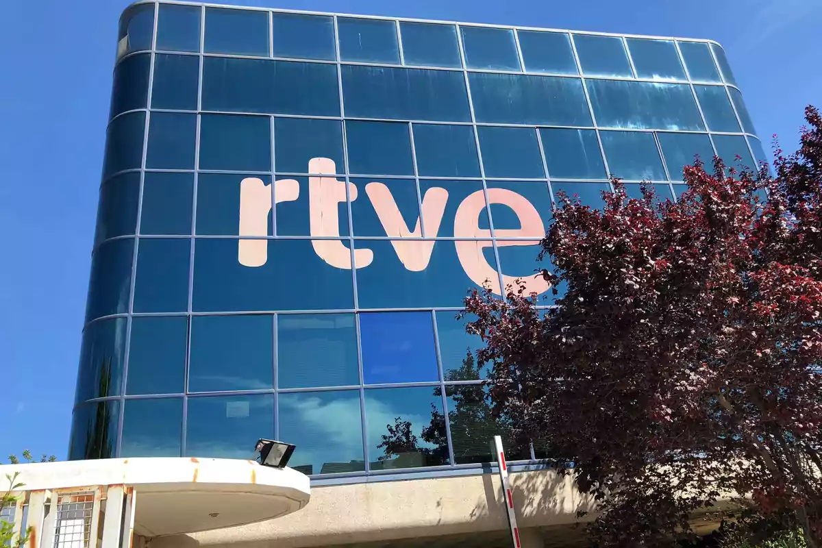 Edificio de cristal con el logo de rtve en la fachada y un árbol en primer plano