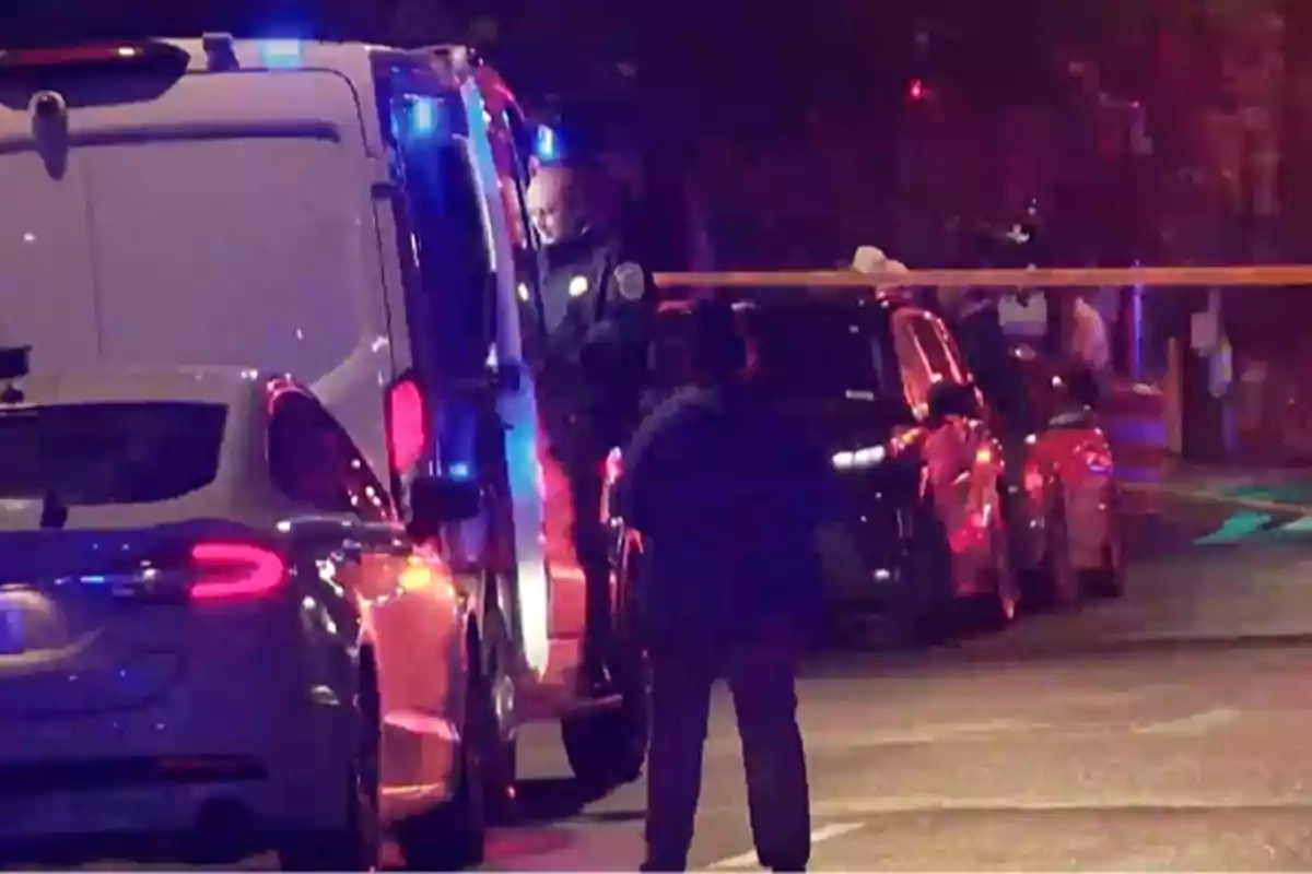 Una escena nocturna muestra a varios vehículos de policía con luces encendidas y oficiales trabajando en un área acordonada. Una escena nocturna muestra a varios vehículos de policía con luces encendidas y oficiales trabajando en un área acordonada.