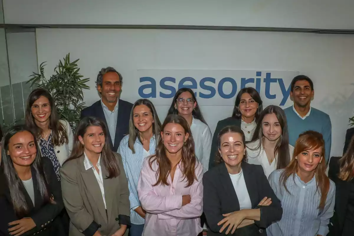 Un grupo de personas sonrientes posando frente a un cartel que dice "asesority" en una oficina.