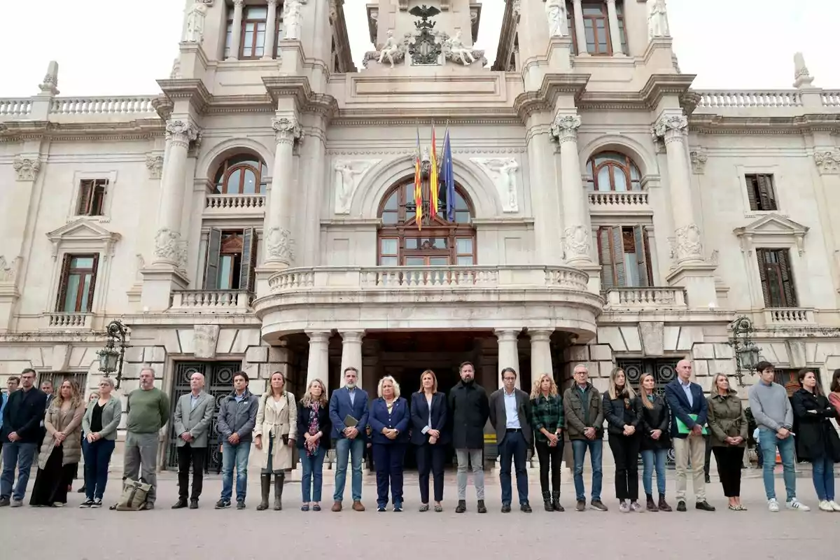 Un grupo de personas está de pie frente a un edificio histórico con columnas y banderas en la fachada.