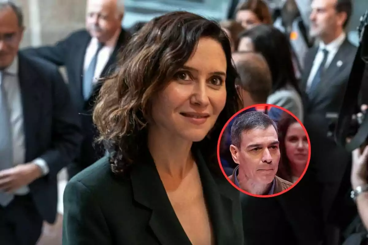 A woman with dark curly brown hair is in the foreground, dressed in a dark suit, while in the background there are several blurred people; in the bottom right corner, there is a red circle with the face of a man.