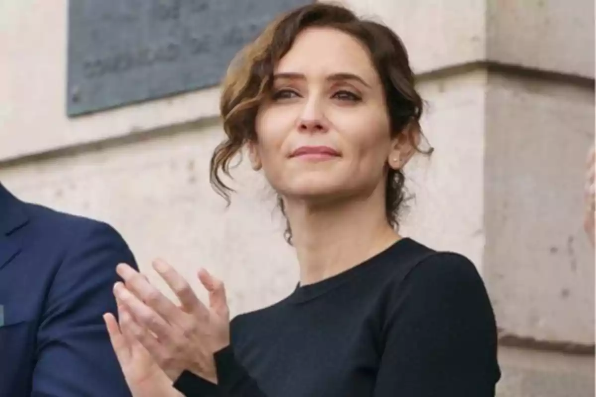 Woman with wavy brown hair clapping in front of a stone wall.