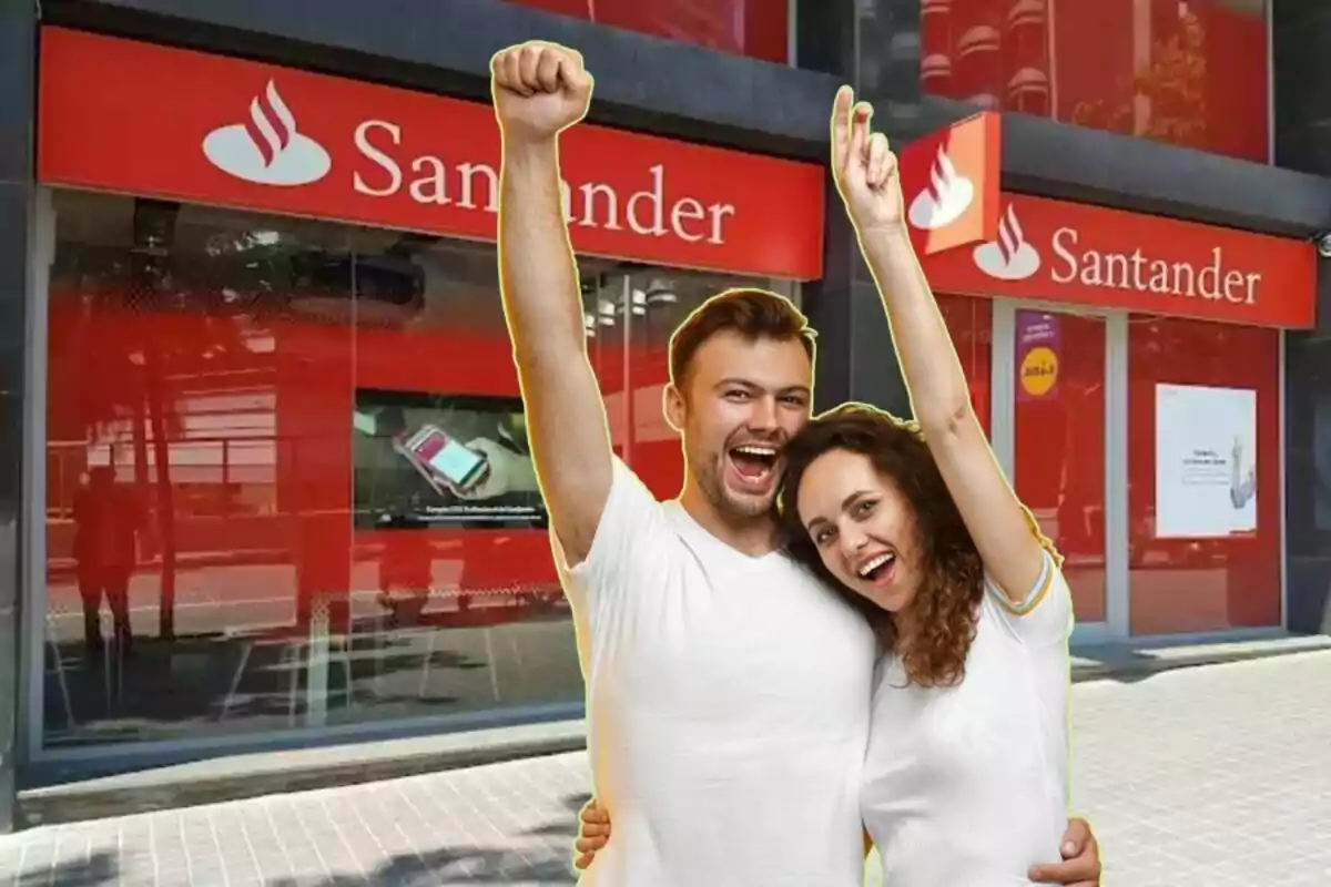 Una pareja sonriente levanta los brazos frente a una sucursal de banco con letreros rojos.