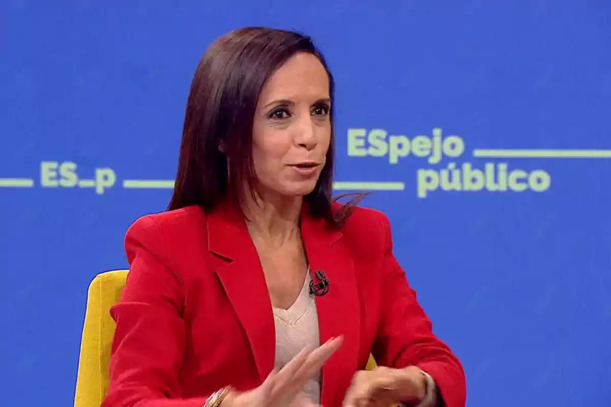 Mujer con chaqueta roja hablando en un programa de televisión con fondo azul. Mujer con chaqueta roja hablando en un programa de televisión con fondo azul.