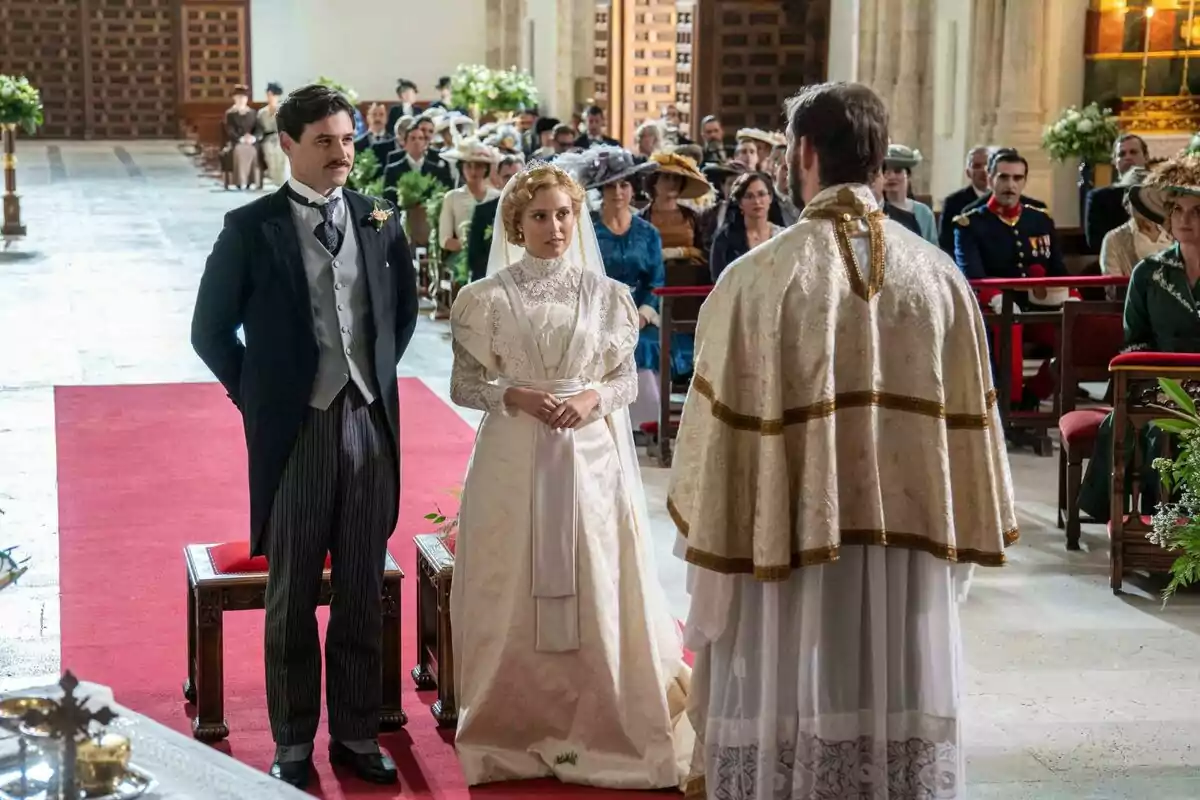 Arturo Sancho y Ana Garcés vestidos de época está de pie frente a un sacerdote en una ceremonia de boda en una iglesia, rodeados de invitados sentados, en La Promesa.