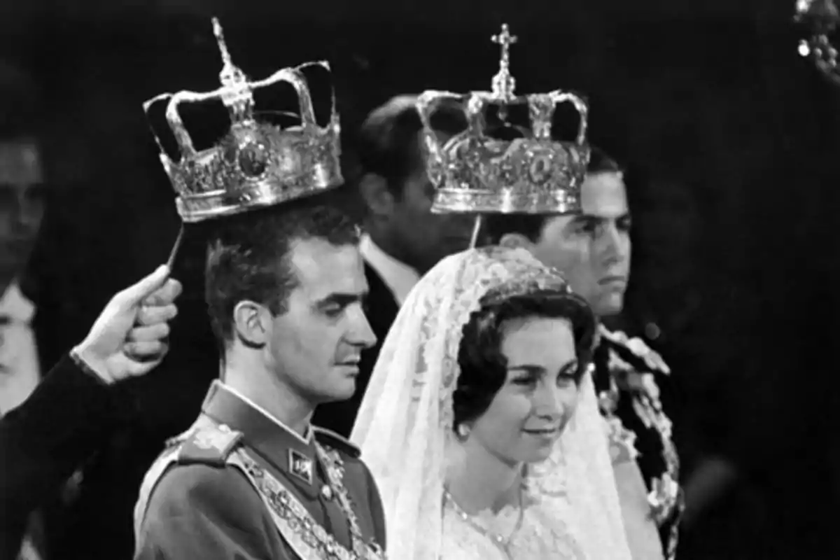 Juan Carlos I y la reina Sofía vestida de manera formal está en una ceremonia, con coronas sostenidas sobre sus cabezas. Juan Carlos I y la reina Sofía vestida de manera formal está en una ceremonia, con coronas sostenidas sobre sus cabezas.