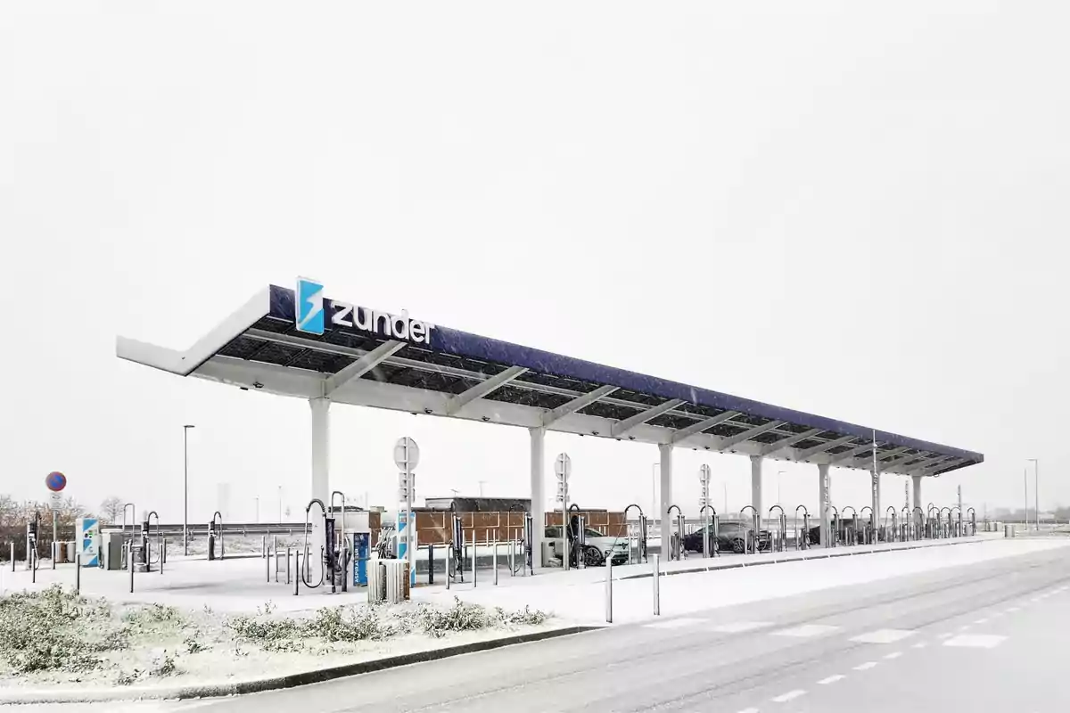 Estación de carga para vehículos eléctricos cubierta de nieve con un techo solar y el logotipo de Zunder.