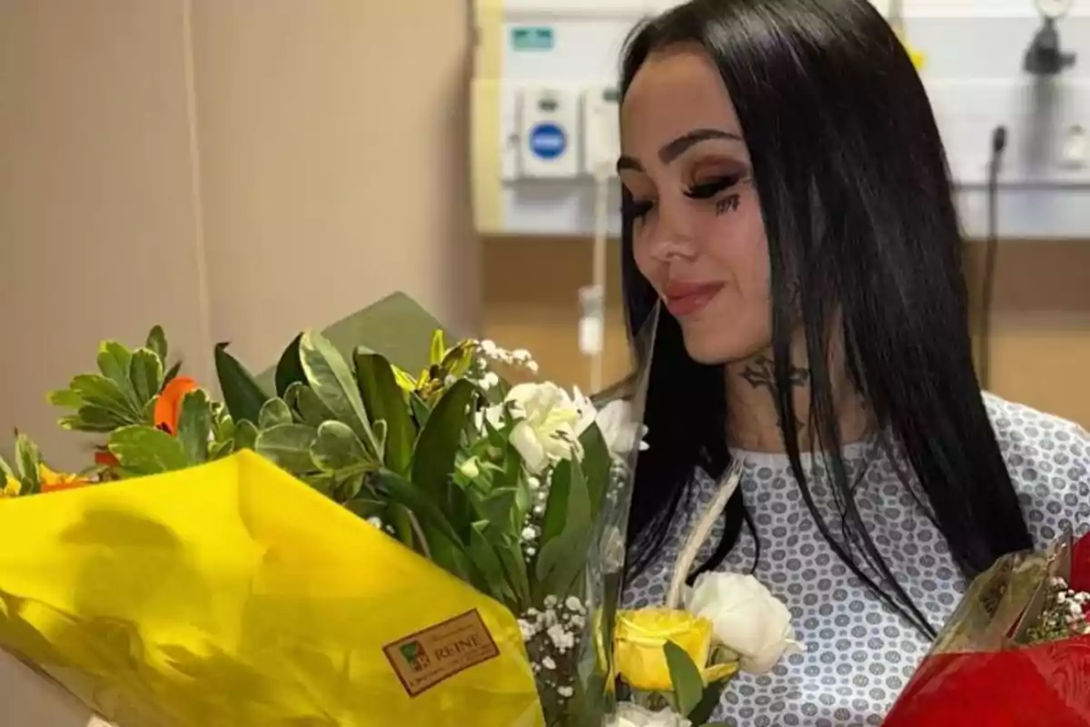 Una mujer con cabello oscuro sostiene un ramo de flores coloridas mientras sonríe y mira hacia abajo. Una mujer con cabello oscuro sostiene un ramo de flores coloridas mientras sonríe y mira hacia abajo.