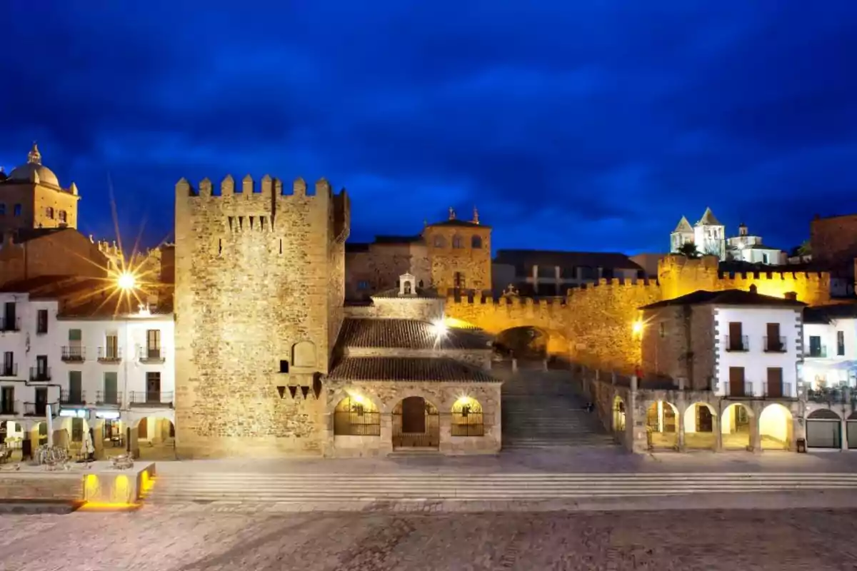 Plaza mayor de Cáceres iluminada al anochecer con edificios históricos y cielo azul intenso