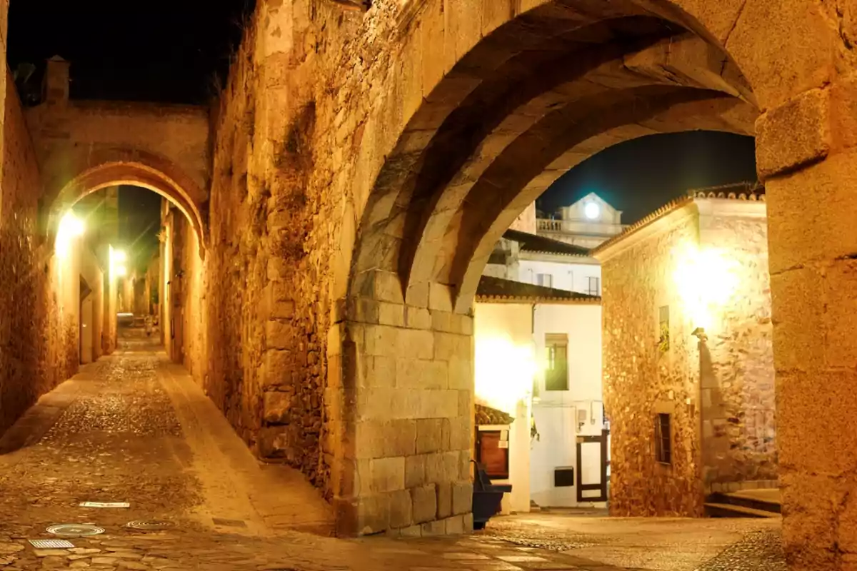 Callejón empedrado y arco de piedra iluminados por faroles en un casco antiguo durante la noche Callejón empedrado y arco de piedra iluminados por faroles en un casco antiguo durante la noche