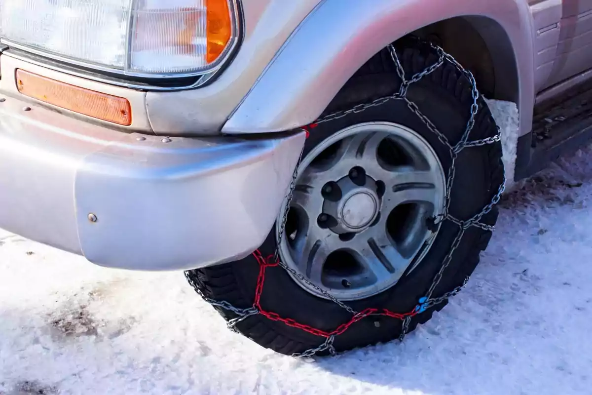 Neumático de un vehículo con cadenas para nieve en una carretera nevada.