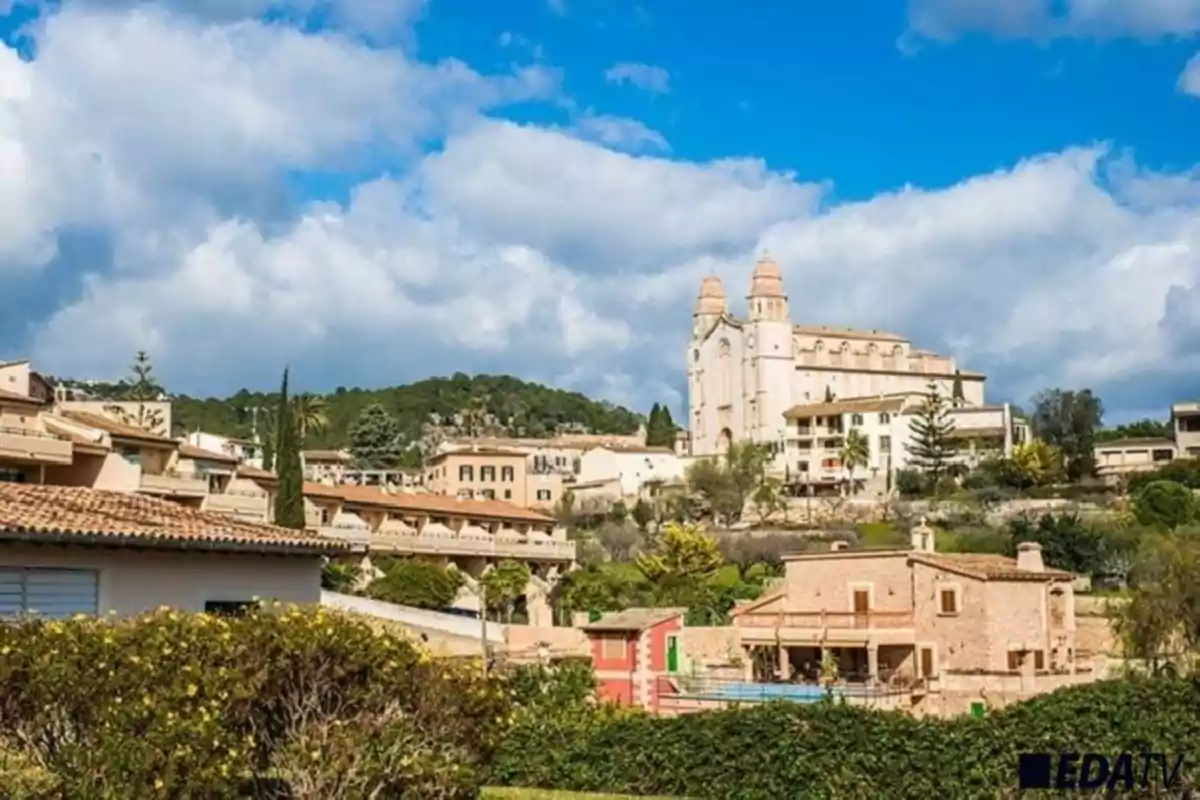 Vista panorámica de un pueblo con una iglesia en una colina bajo un cielo azul con nubes.