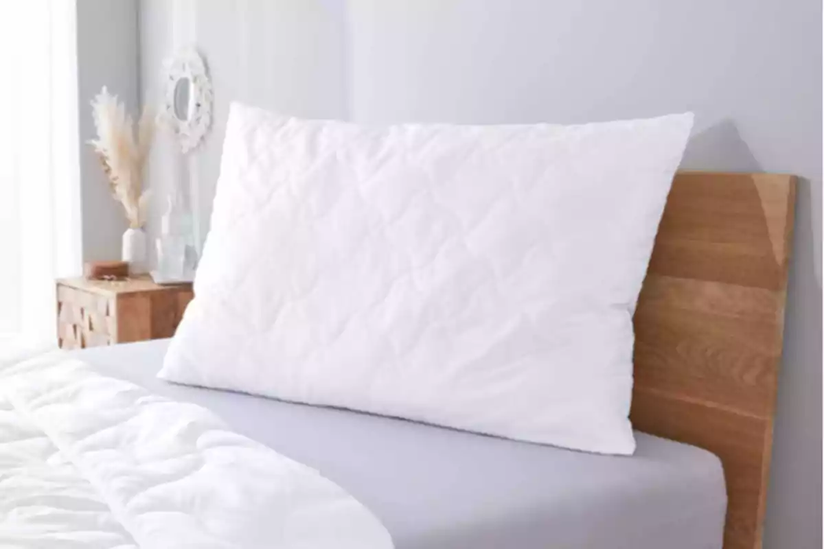 Almohada blanca sobre una cama con cabecera de madera en una habitación decorada con tonos claros Almohada blanca sobre una cama con cabecera de madera en una habitación decorada con tonos claros