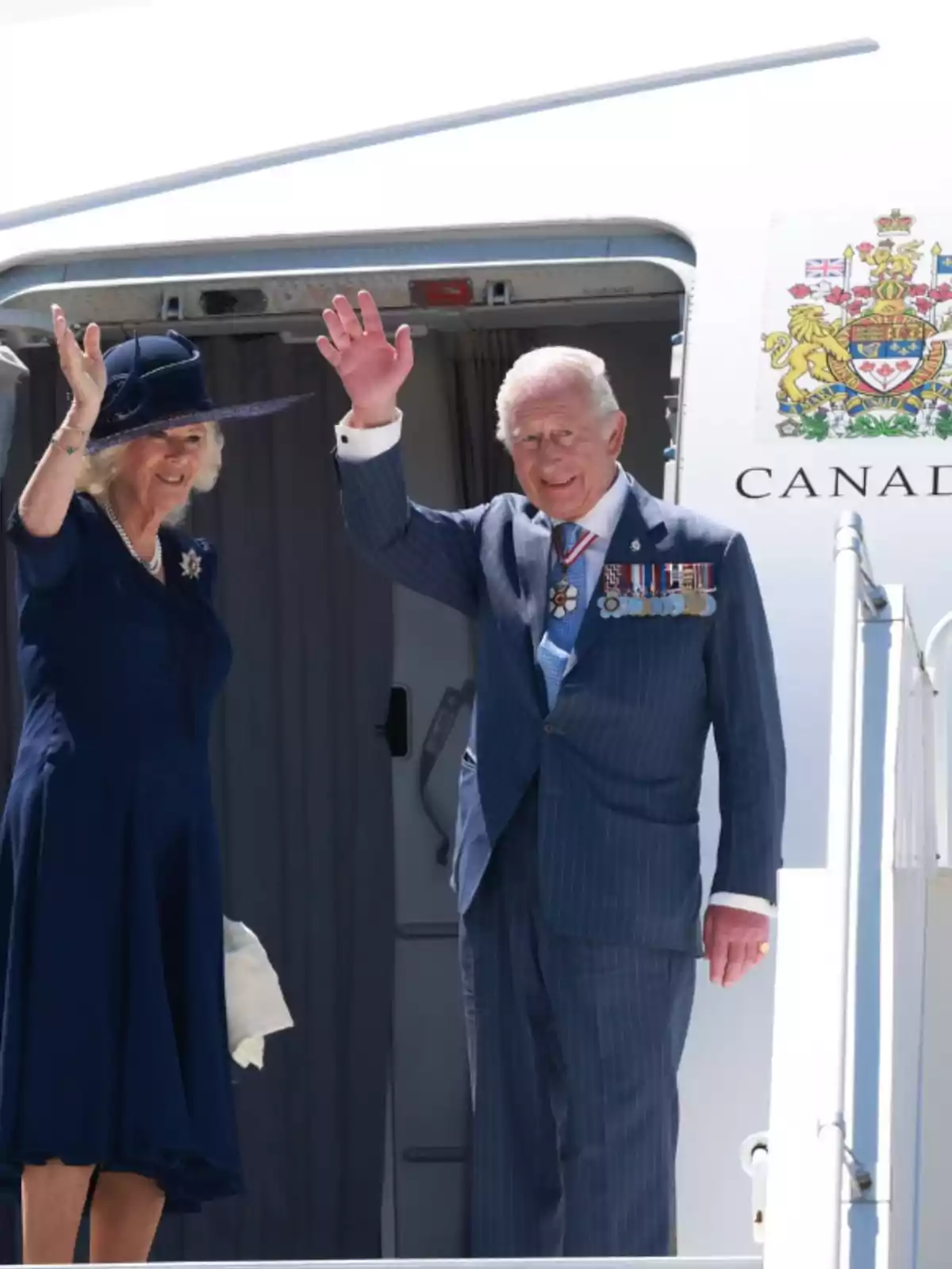 A well-dressed couple waves from the door of a plane with the Canadian emblem visible on the side. A well-dressed couple waves from the door of a plane with the Canadian emblem visible on the side.