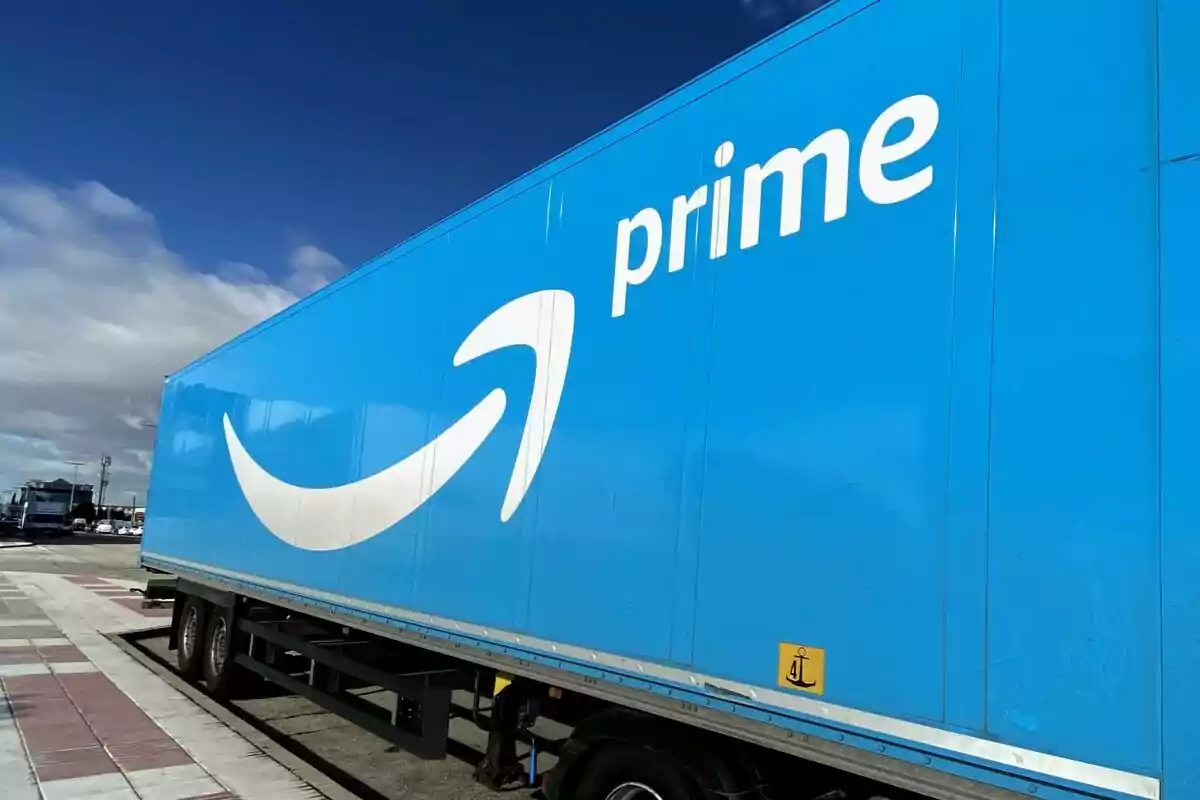 A blue truck with the Amazon logo in a parking lot under a partly cloudy sky.
