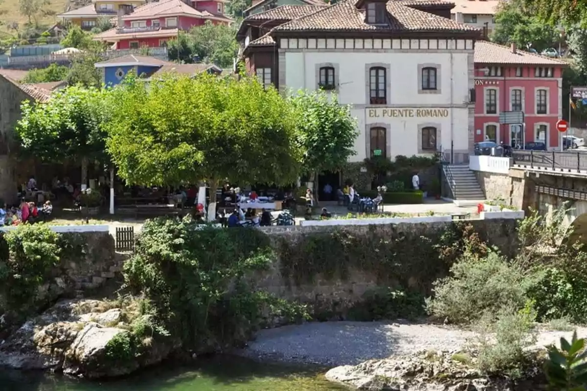 A view of a historic building next to a river surrounded by greenery and people enjoying the surroundings.