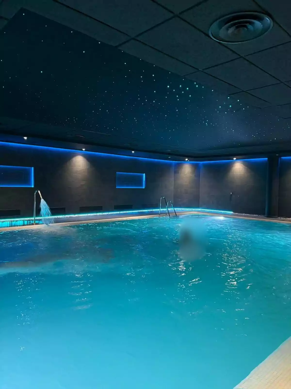 Indoor pool illuminated with blue lights and a starry ceiling.