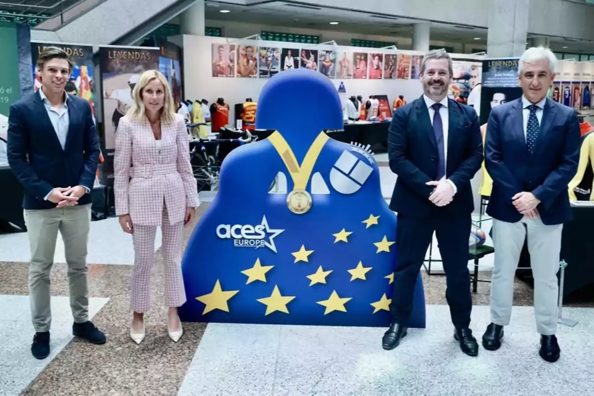 Un grupo de cuatro personas posando junto a una figura azul con estrellas amarillas y un logotipo que dice "aces EUROPE" en un evento en un recinto cerrado.