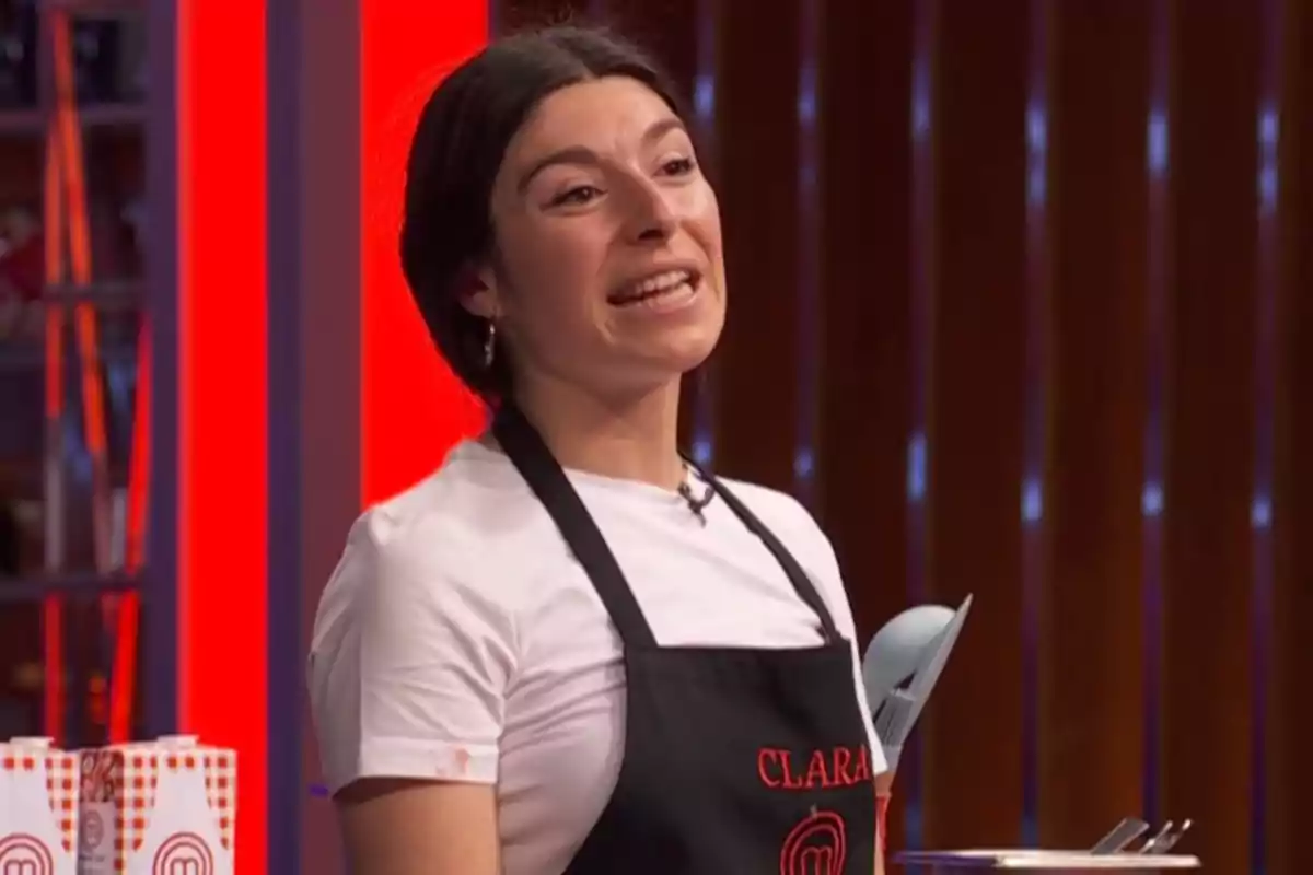 Clara con delantal negro y camiseta blanca participando en 'Masterchef' mientras sonríe y habla Clara con delantal negro y camiseta blanca participando en 'Masterchef' mientras sonríe y habla