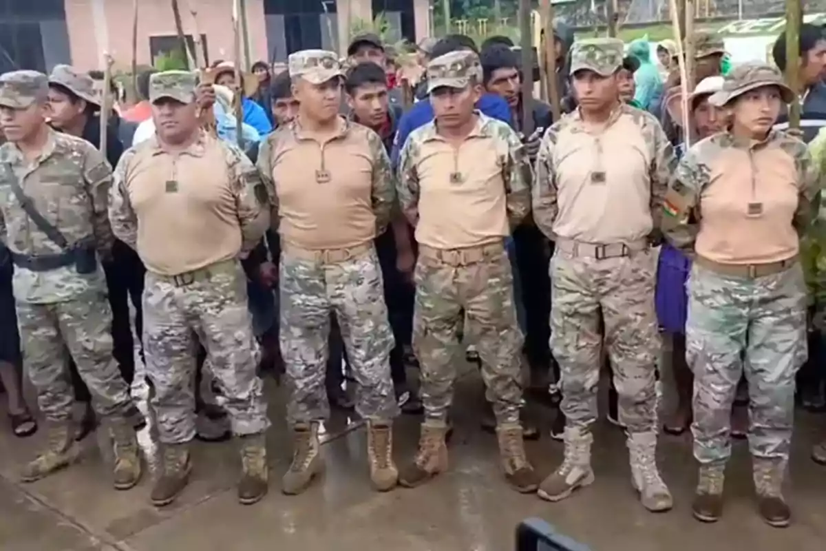 Un grupo de personas vestidas con uniformes militares camuflados está de pie en formación frente a una multitud en un entorno al aire libre.