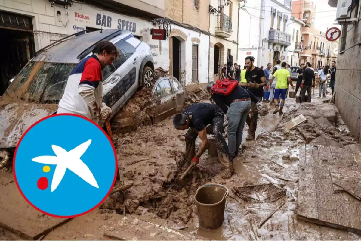 Personas trabajando para limpiar una calle llena de barro tras una inundación, con un coche parcialmente enterrado y un logotipo en la esquina inferior izquierda.