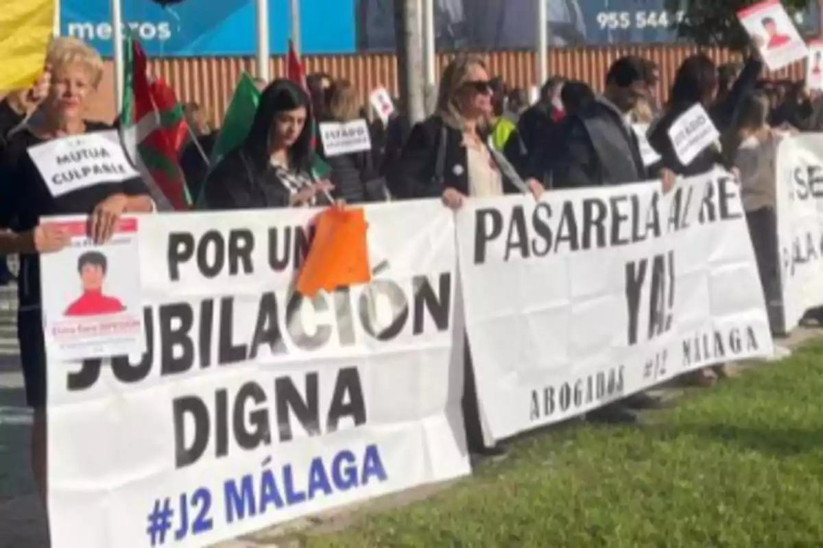 Un grupo de personas sostiene pancartas en una manifestación, con mensajes que piden una jubilación digna y una pasarela al río en Málaga.