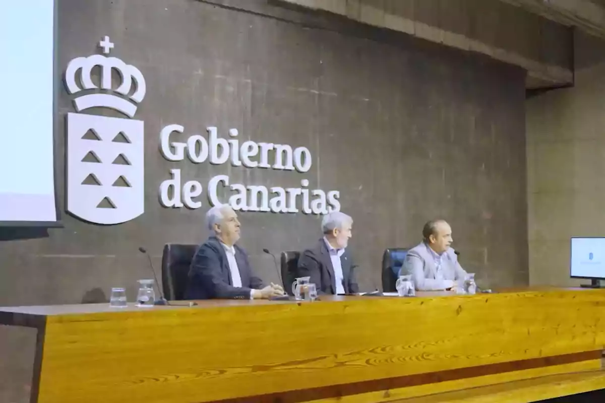 Tres personas sentadas en una mesa de conferencias frente a un cartel que dice "Gobierno de Canarias".