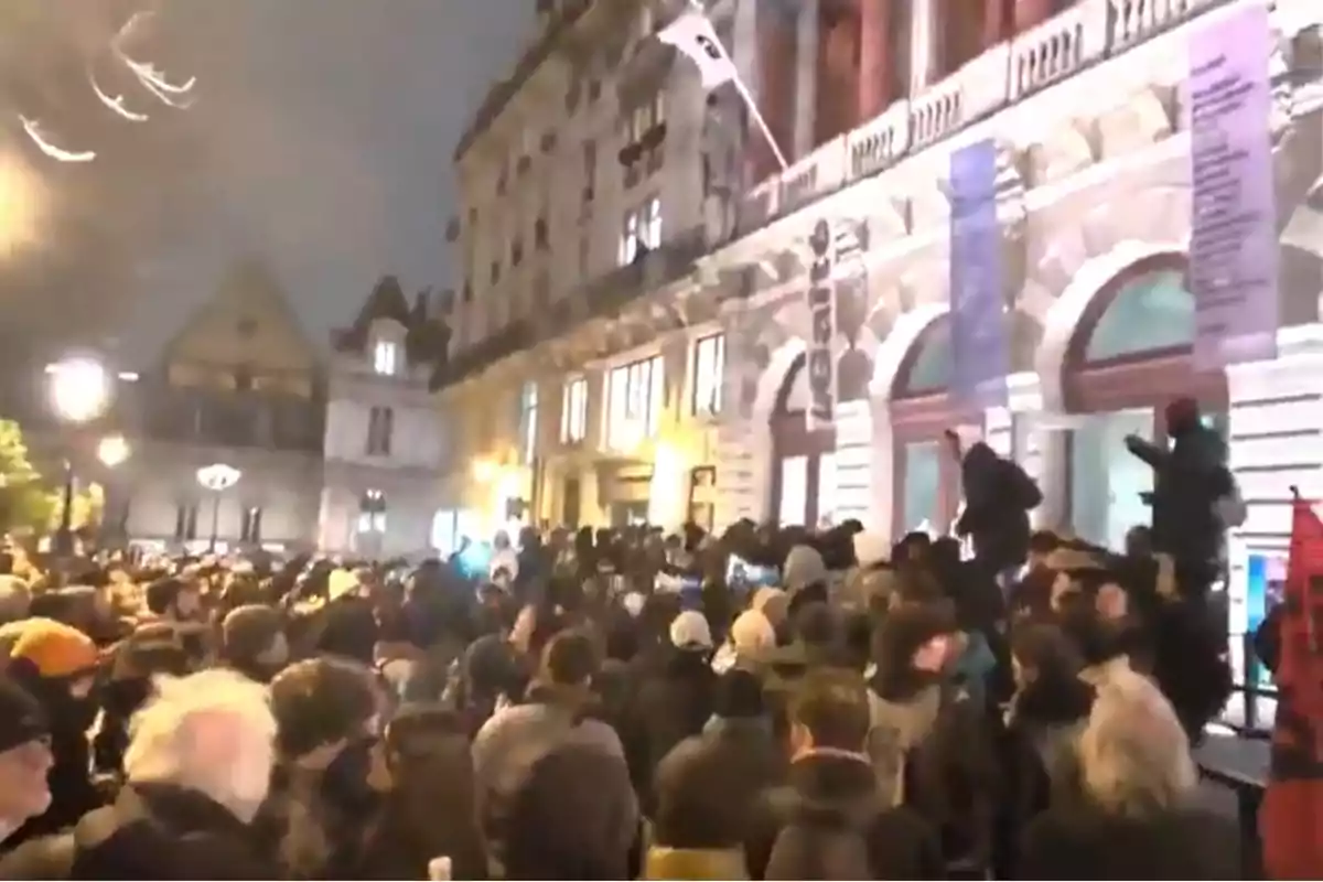 Una multitud se reúne frente a un edificio iluminado durante la noche.