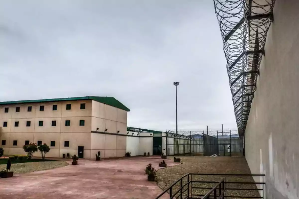 Prison building with high walls and barbed wire under a cloudy sky. Prison building with high walls and barbed wire under a cloudy sky.