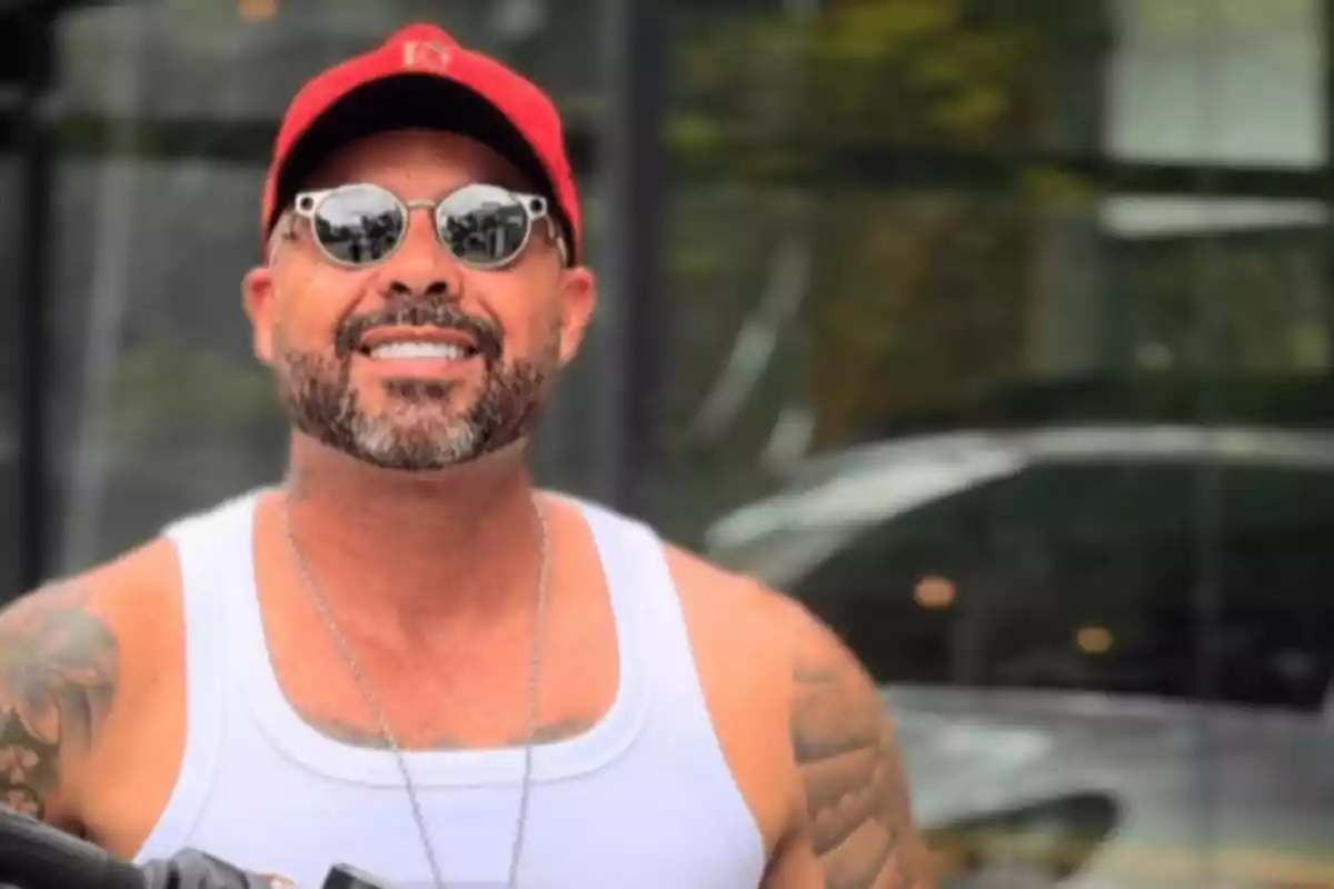 Man in red cap and sunglasses smiling in front of an urban background.