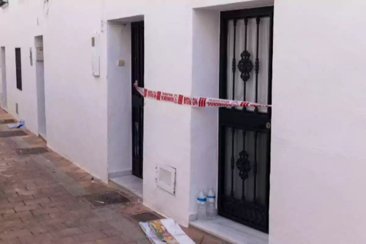 Una puerta de entrada con cinta de precaución en una calle de casas blancas.