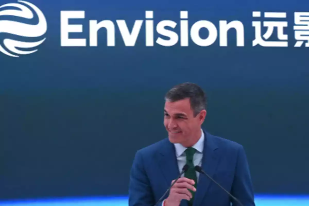 Un hombre en traje azul sonríe mientras habla en un micrófono frente a un fondo con el logotipo de Envision.