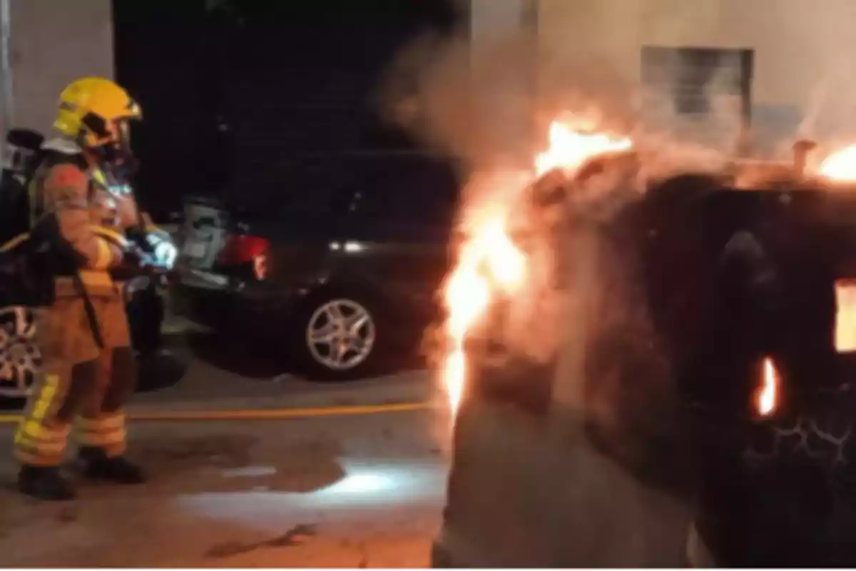 Un bombero con equipo completo observa un contenedor en llamas en una calle durante la noche. Un bombero con equipo completo observa un contenedor en llamas en una calle durante la noche.
