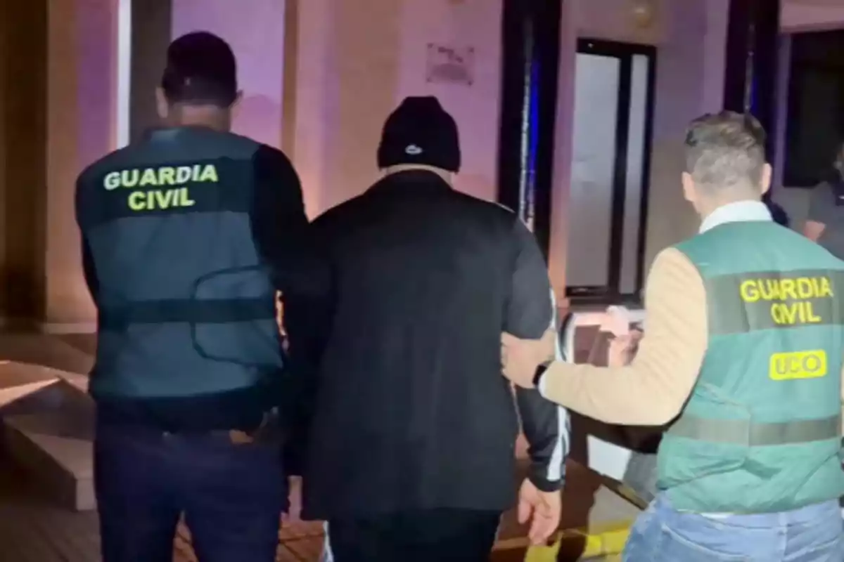 Dos agentes de la Guardia Civil escoltan a una persona vestida de negro en un entorno urbano.