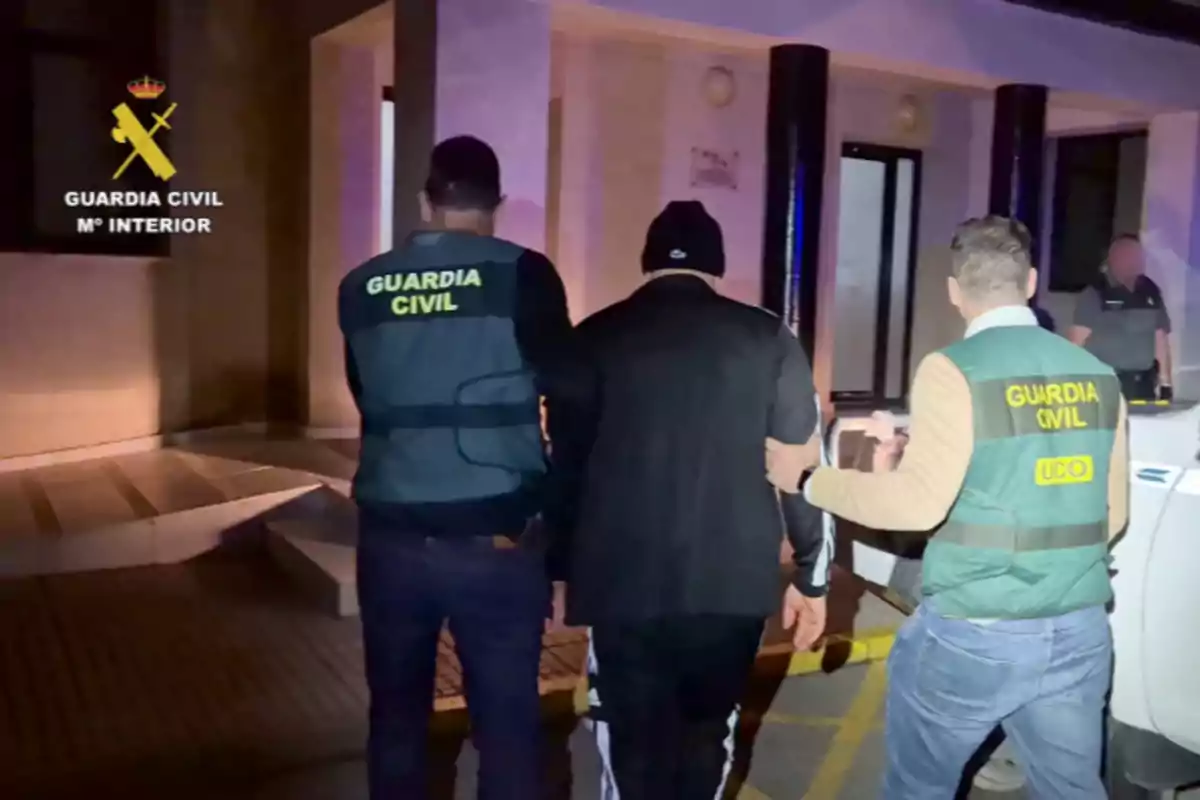 Dos agentes de la Guardia Civil escoltan a una persona hacia un edificio durante la noche. Dos agentes de la Guardia Civil escoltan a una persona hacia un edificio durante la noche.