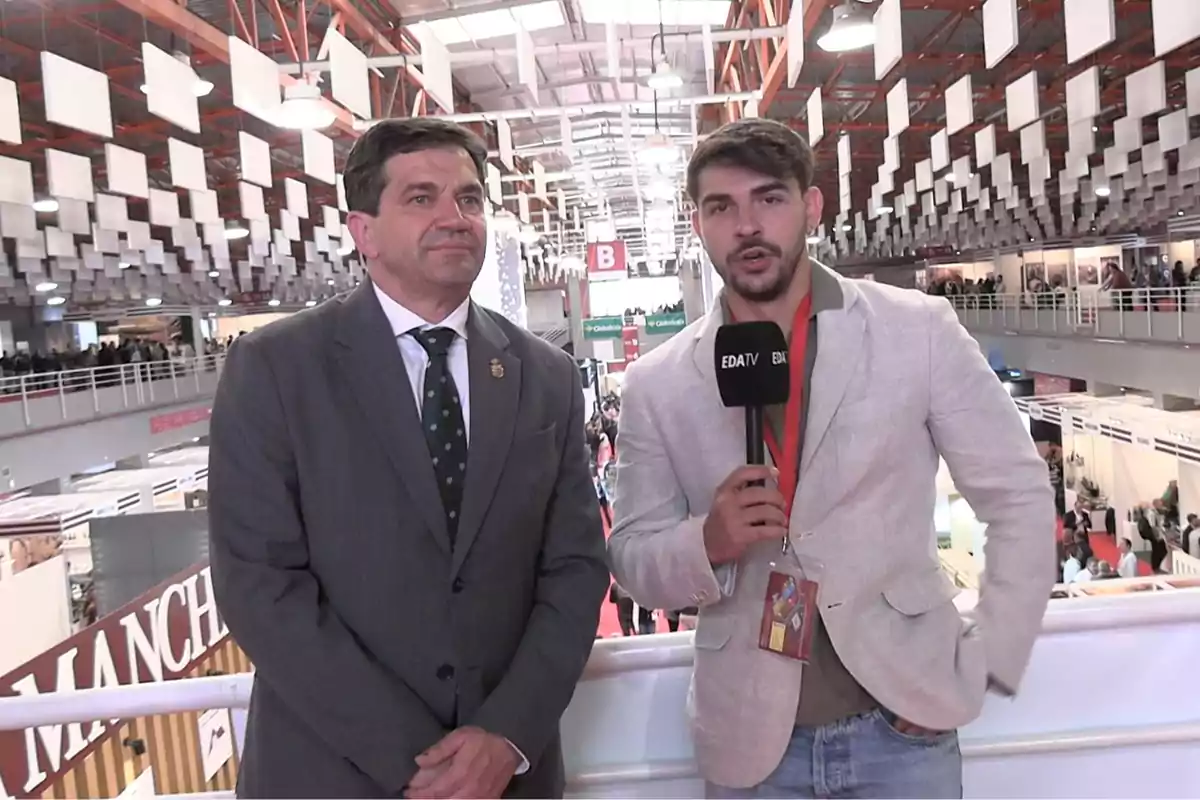 Dos hombres de pie en un evento con un micrófono de EDATV en un entorno de feria o exposición. Dos hombres de pie en un evento con un micrófono de EDATV en un entorno de feria o exposición.