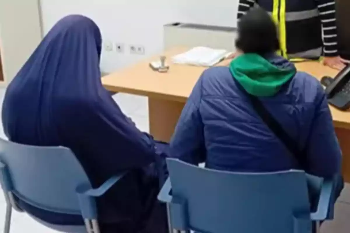 Dos personas sentadas en sillas frente a un escritorio en una oficina.