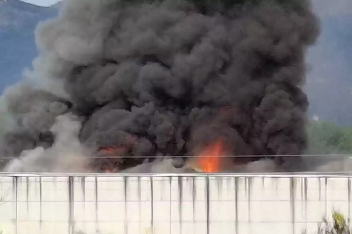 Un gran incendio produce una densa columna de humo negro sobre un edificio industrial.
