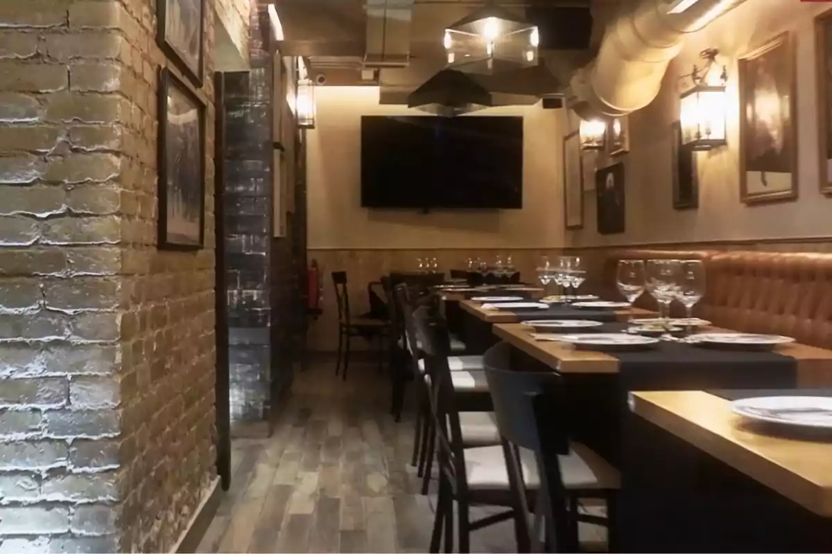 Un restaurante acogedor con paredes de ladrillo expuesto, mesas elegantemente dispuestas con copas y platos, y una pantalla grande en la pared del fondo. Un restaurante acogedor con paredes de ladrillo expuesto, mesas elegantemente dispuestas con copas y platos, y una pantalla grande en la pared del fondo.