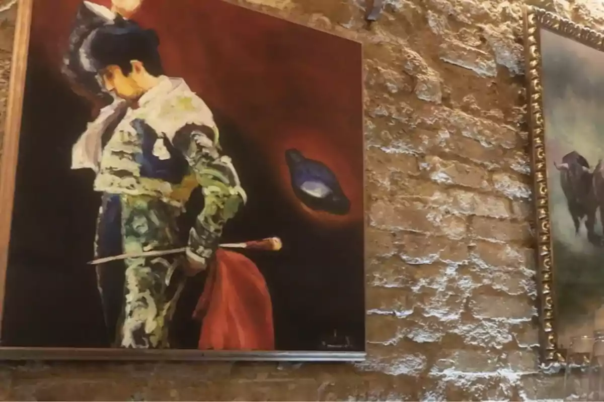 Un cuadro de un torero con traje de luces sosteniendo una muleta roja en una pared de ladrillo. Un cuadro de un torero con traje de luces sosteniendo una muleta roja en una pared de ladrillo.